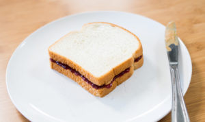 peanut butter and jelly sandwich on plate with butter knife covered in peanut butter